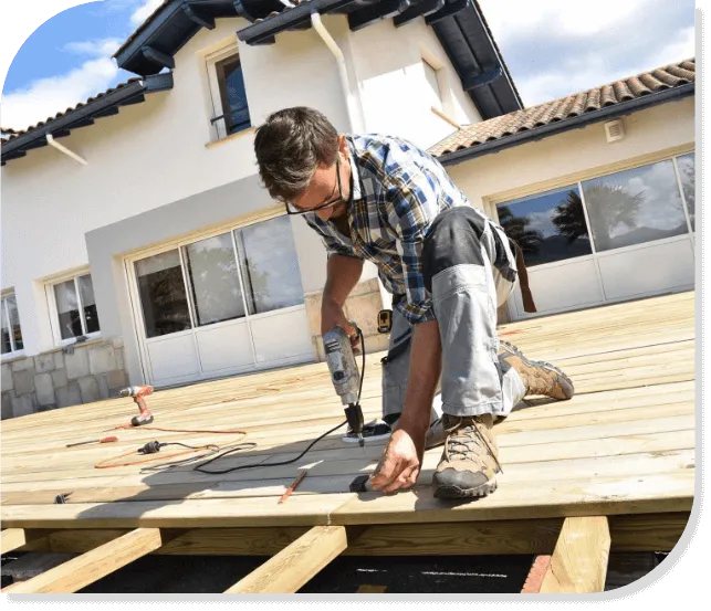 Installer kneeling on a deck frame, fastening boards over the joists with a drill